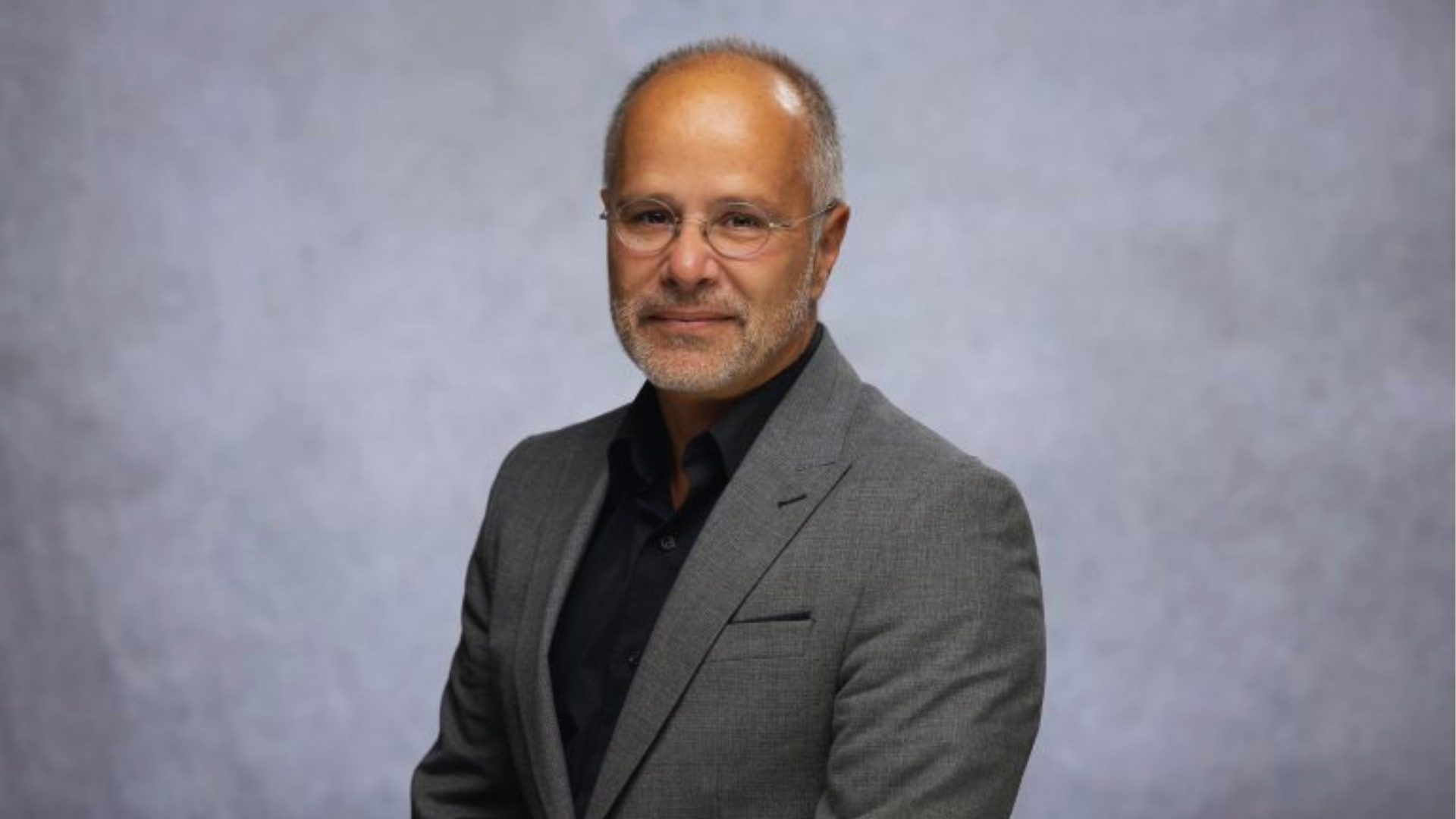 Balding middle-aged man wearing a suit and glasses.
