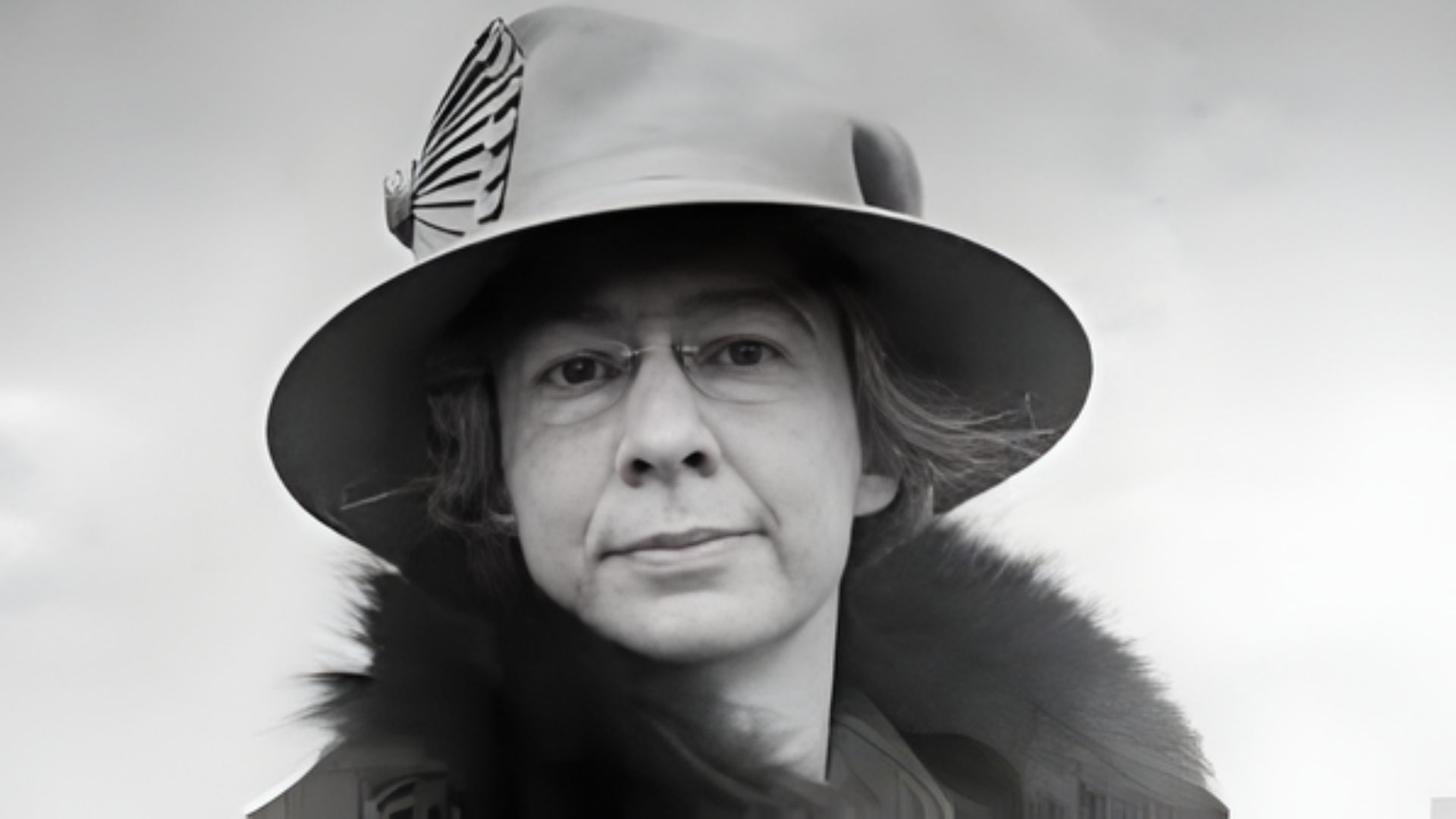 A woman wearing a stylish hat and glasses, smiling softly at the camera.