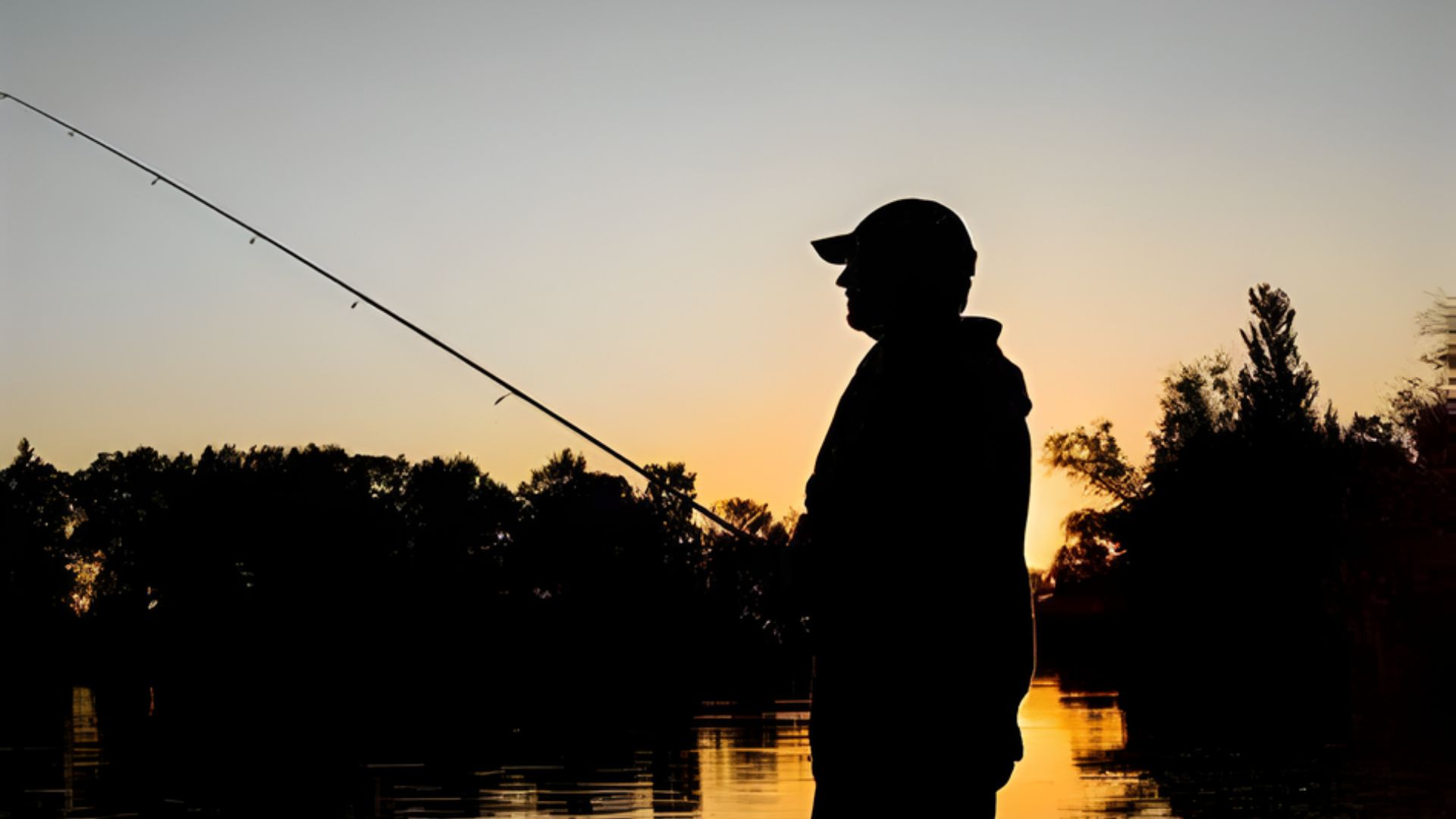 Silhouette of a man fishing against a vibrant sunset, with hues of orange and purple illuminating the sky.