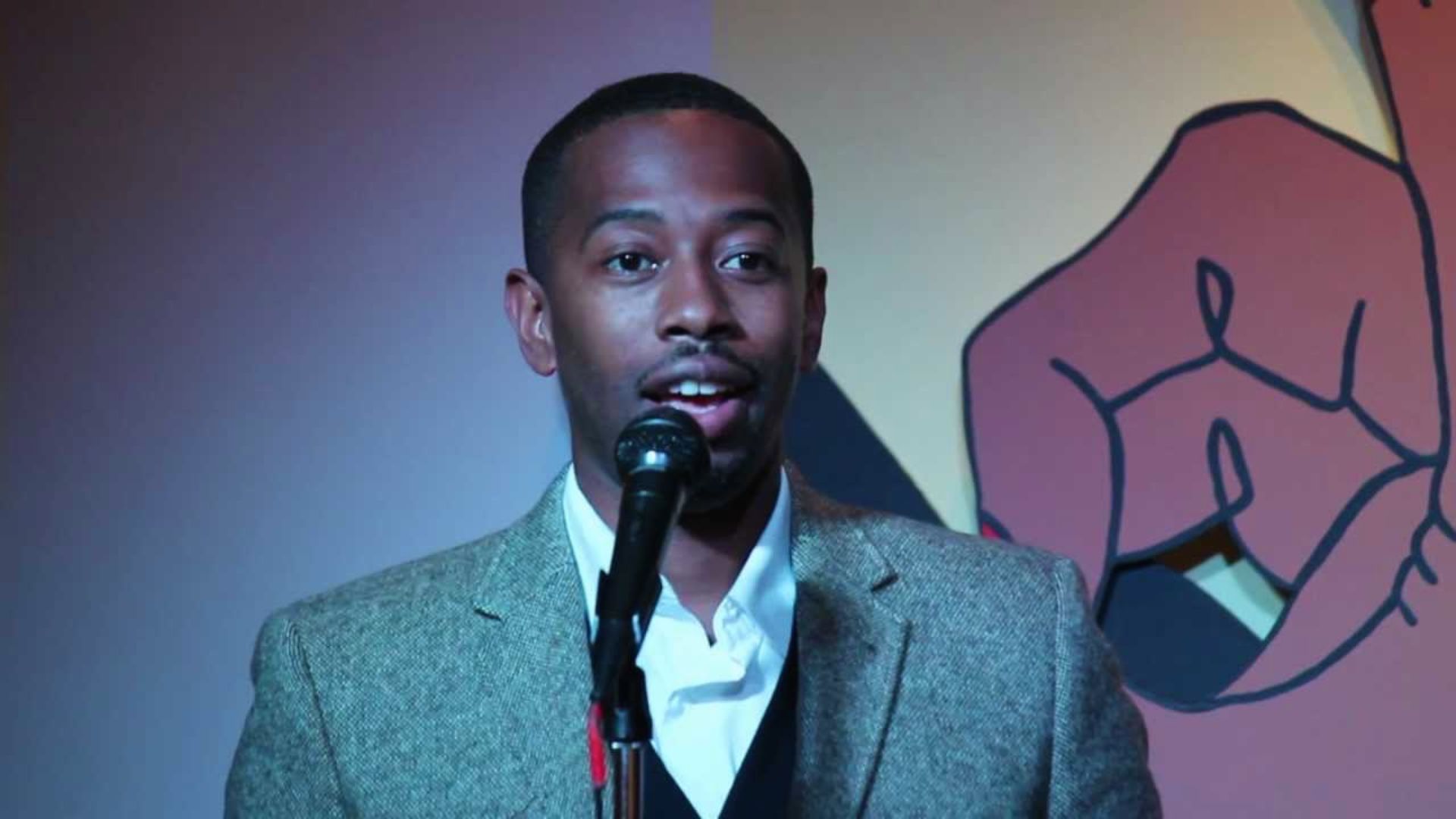 A man in a suit speaks into a microphone during a formal event.