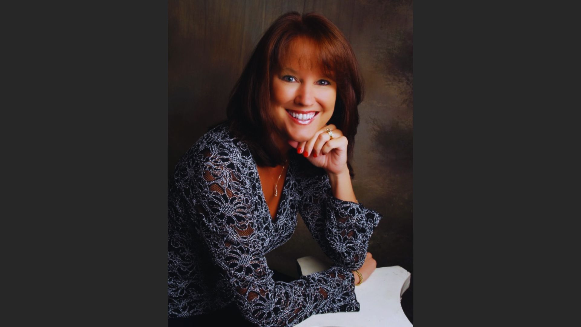 A woman with brown hair wearing a gray shirt, looking directly at the camera with a neutral expression.