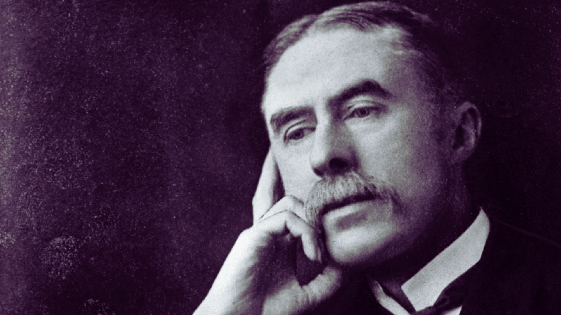 Black and white photo of a man with a prominent mustache, looking directly at the camera with a serious expression.