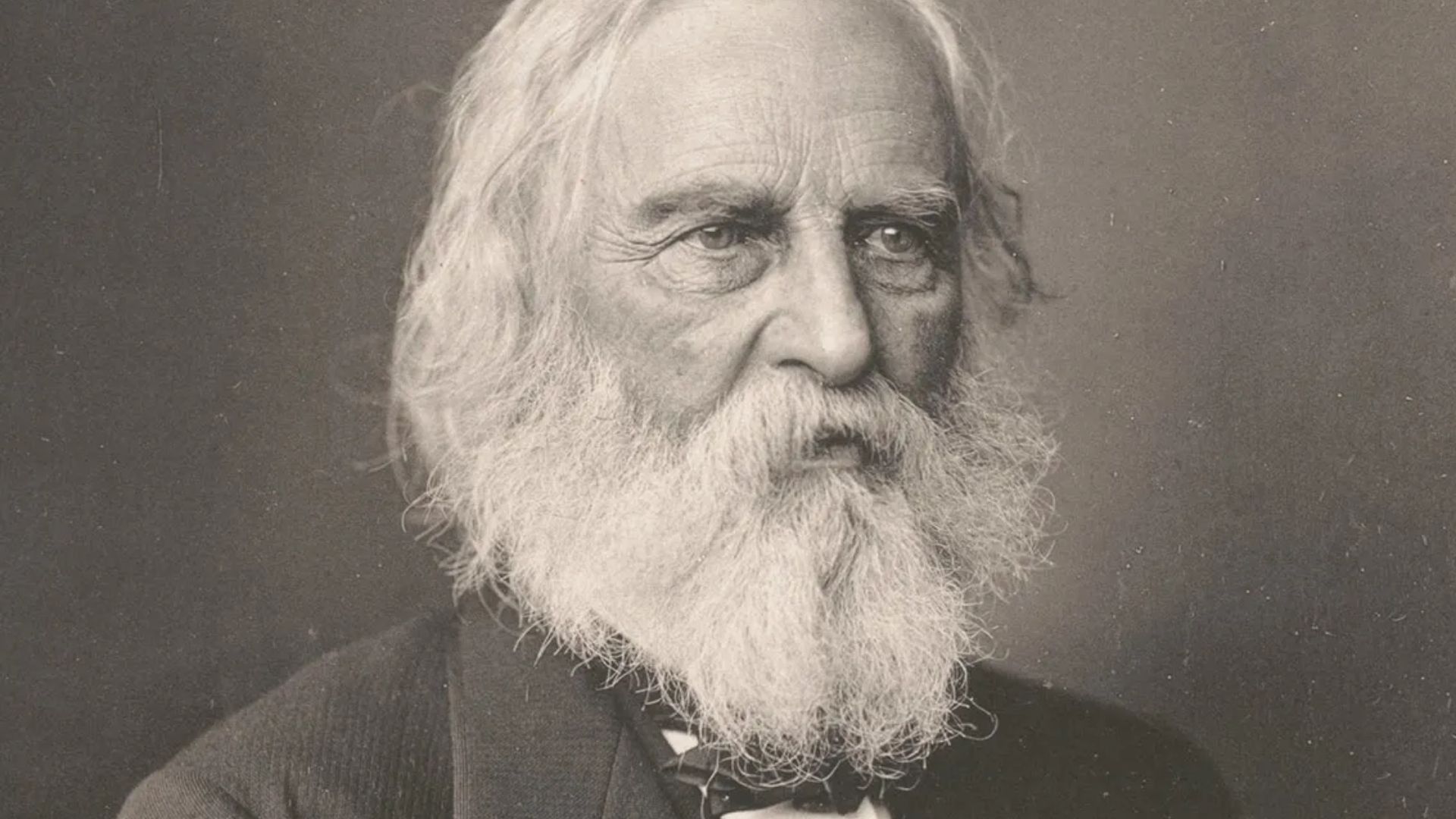 Vintage sepia portrait of Henry Wadsworth Longfellow, older man with long white hair and full white beard in dark coat.
