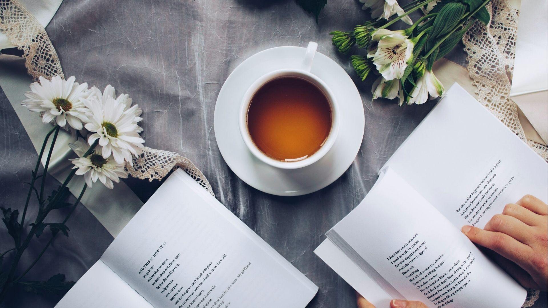 Open poetry book with tea cup and white flowers on table, creating cozy reading atmosphere for literature analysis