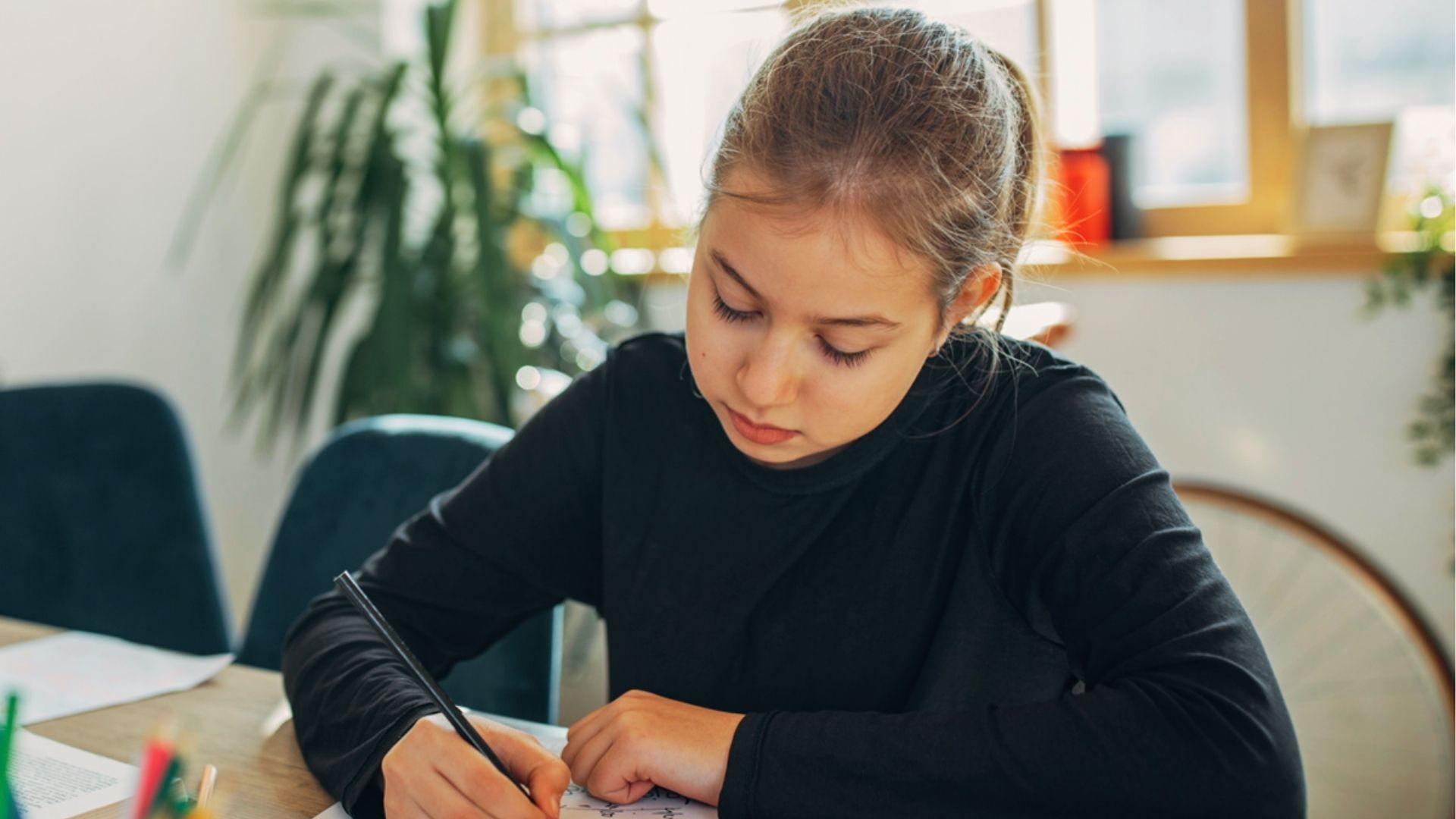 Young girl in black shirt focused on writing poetry at desk, demonstrating how rhythm develops through careful drafting and revision.