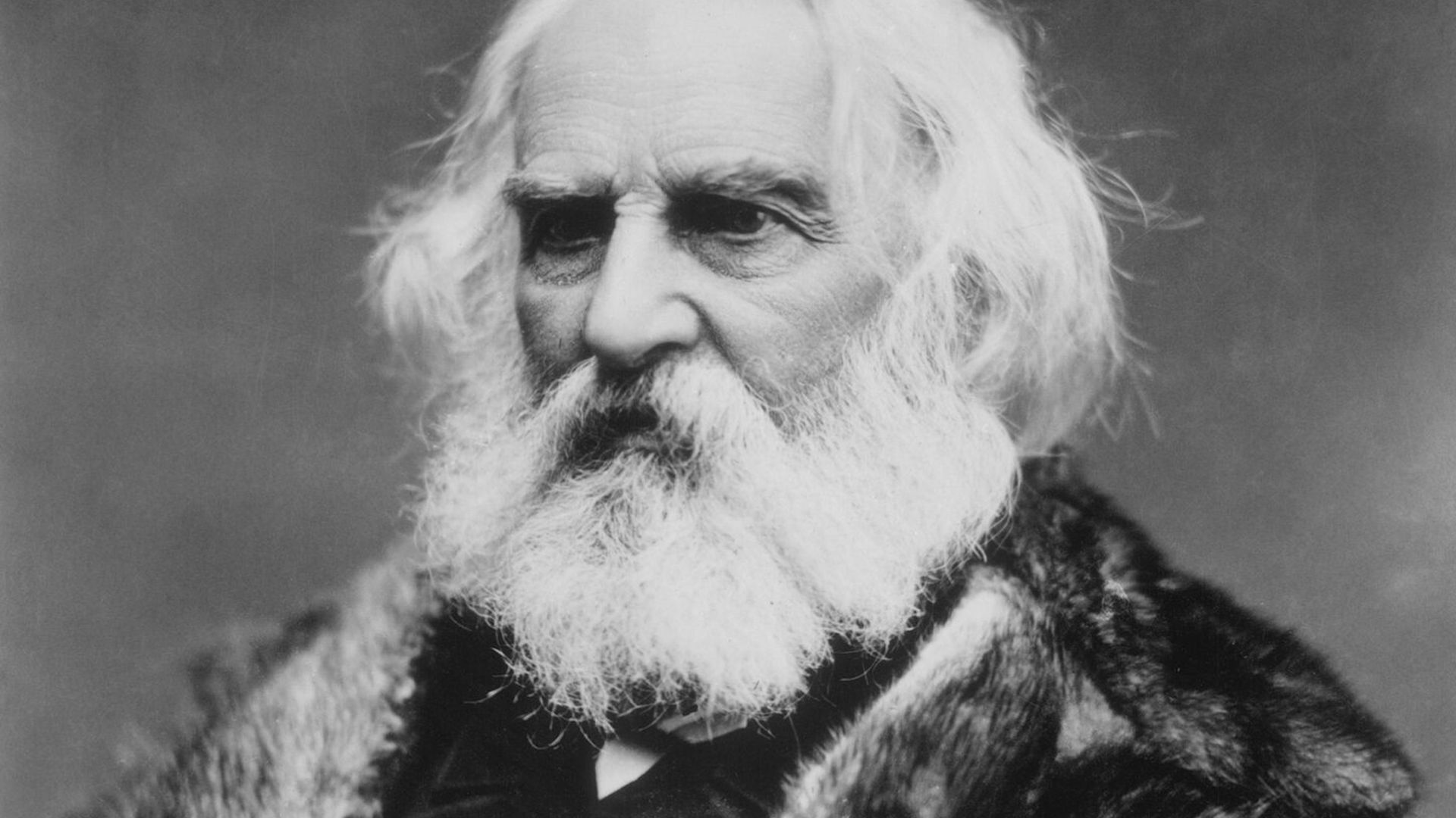 Black and white portrait of poet Henry Wadsworth Longfellow with white beard and fur collar.