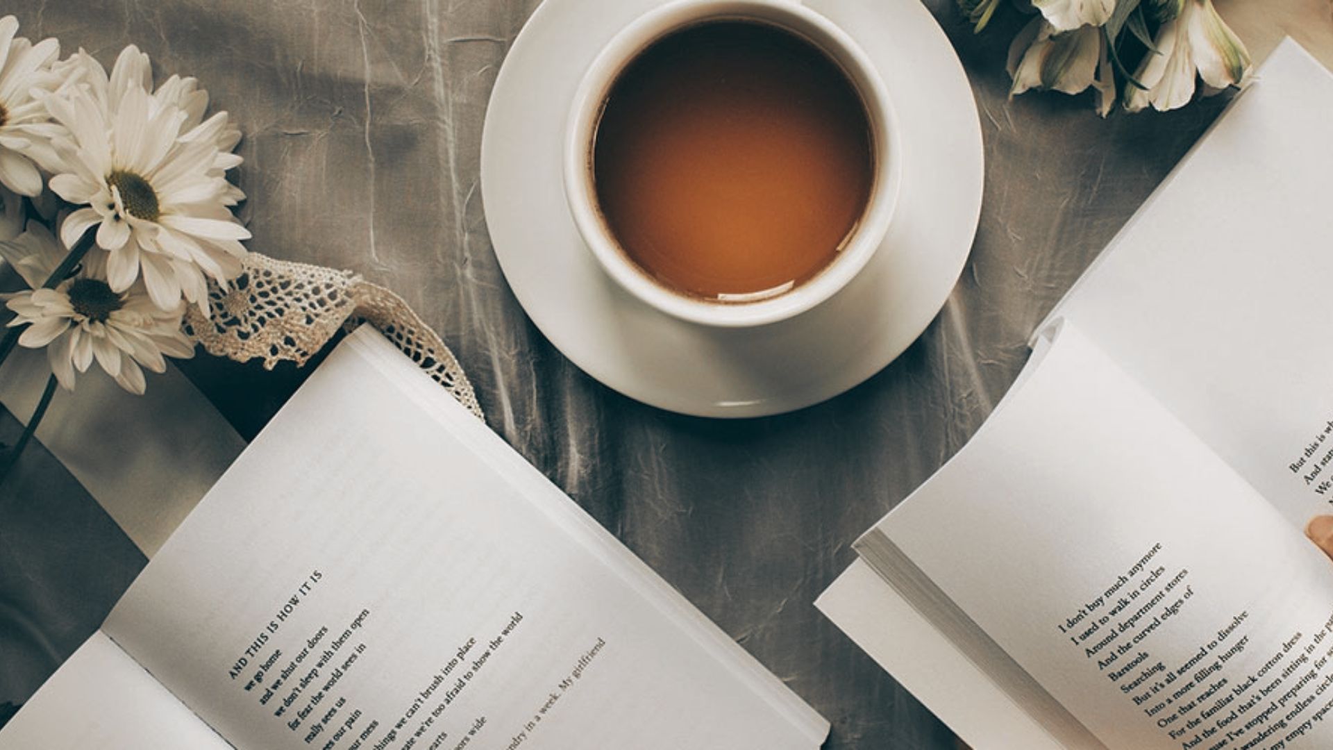 Open poetry books rest beside a warm cup of coffee and fresh daisies on a soft surface.