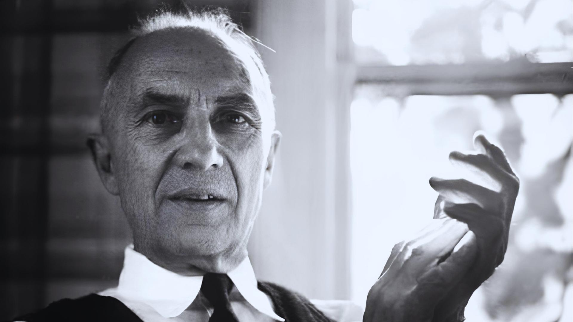Black and white portrait of older man in vest and tie gesturing with hand near window.