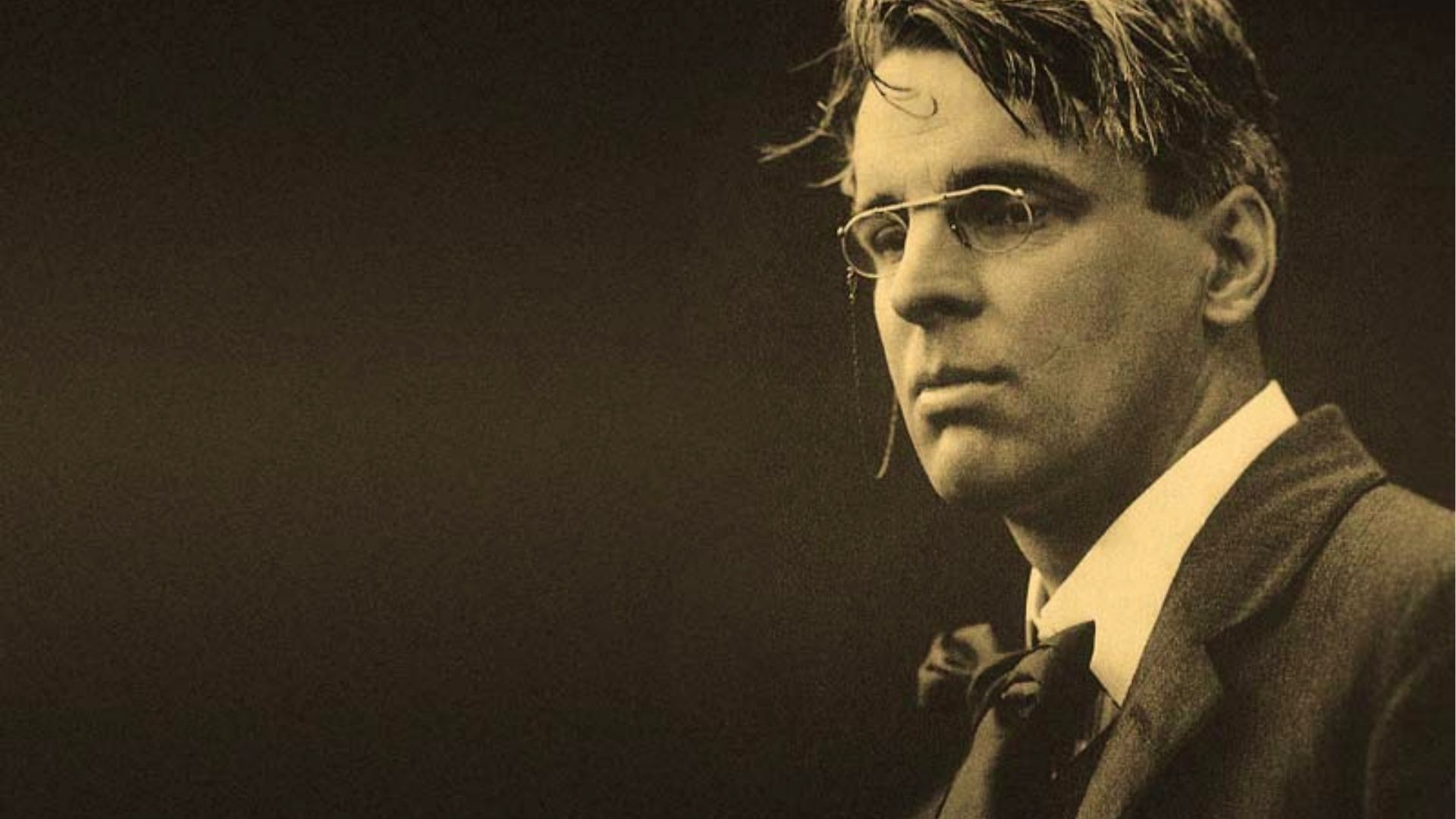 Sepia portrait of W.B. Yeats wearing pince-nez glasses and a bow tie, gazing intensely sideways.