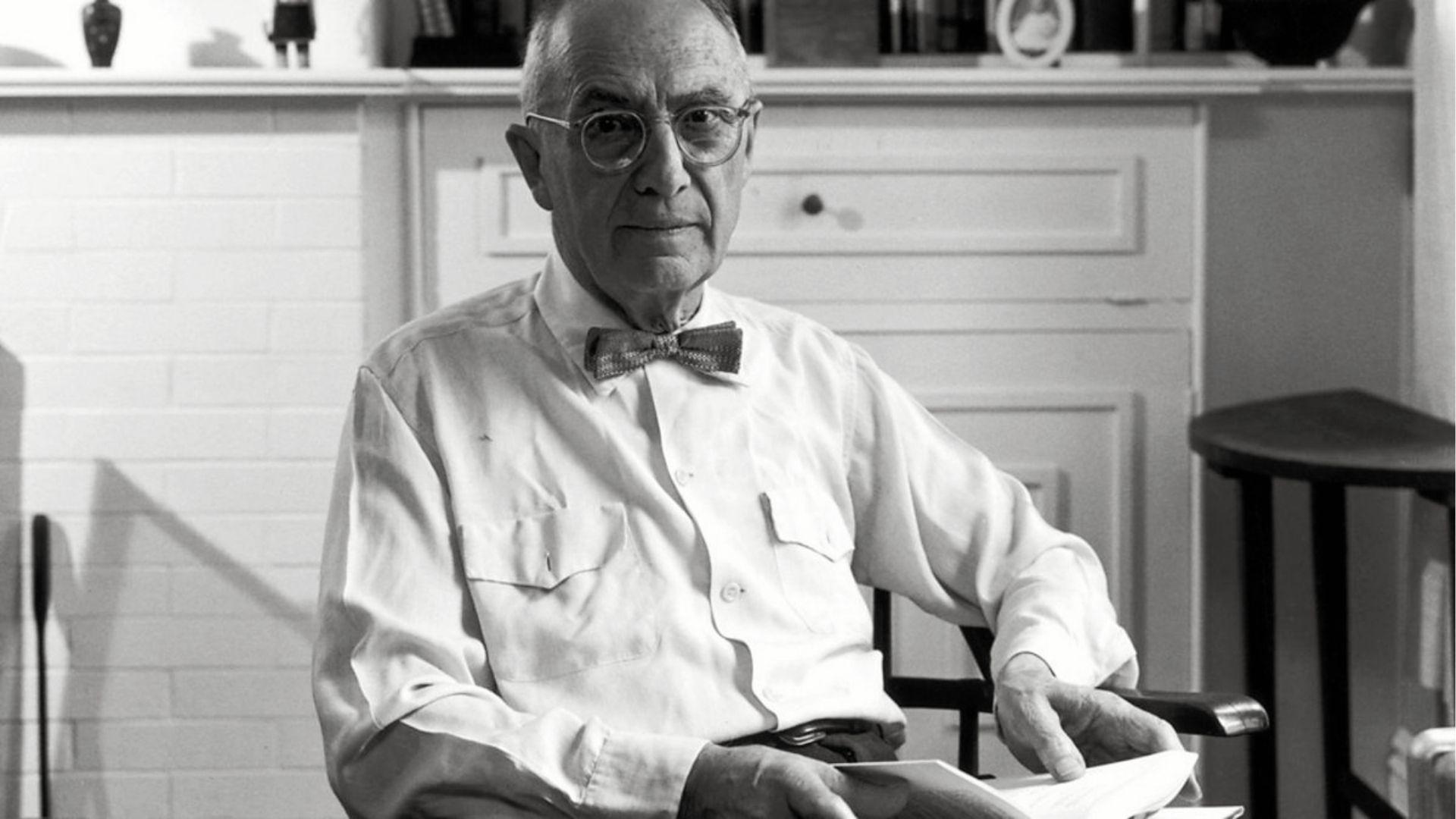 Black-and-white portrait of an elderly poet seated indoors holding papers