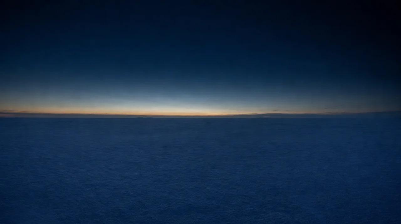 Vast snow-covered plain under dark blue twilight sky with faint orange glow on horizonFile name: vast-snow-plain-twilight-horizon-glow