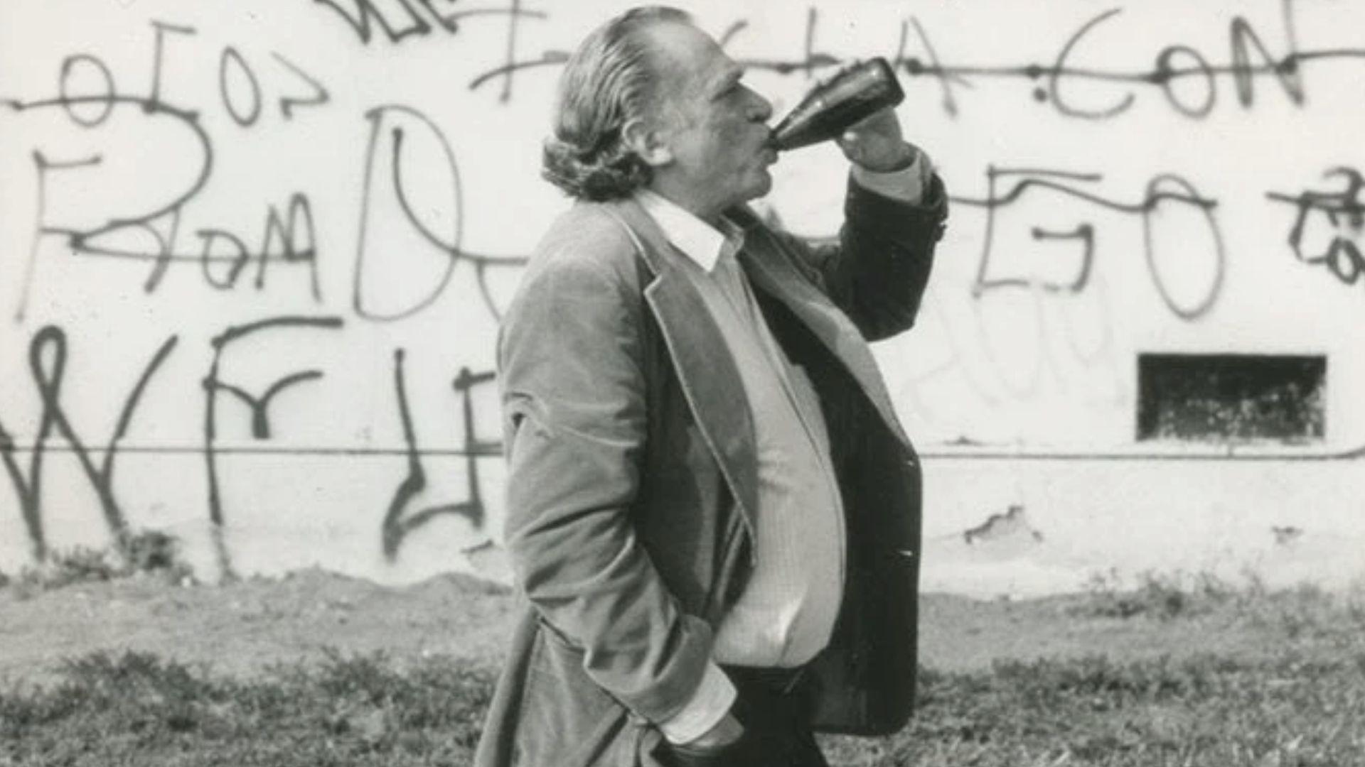 Older man in a suit drinking from a bottle before a graffiti wall File Name: older-man-suit-drinking-bottle-graffiti-wall-black-white