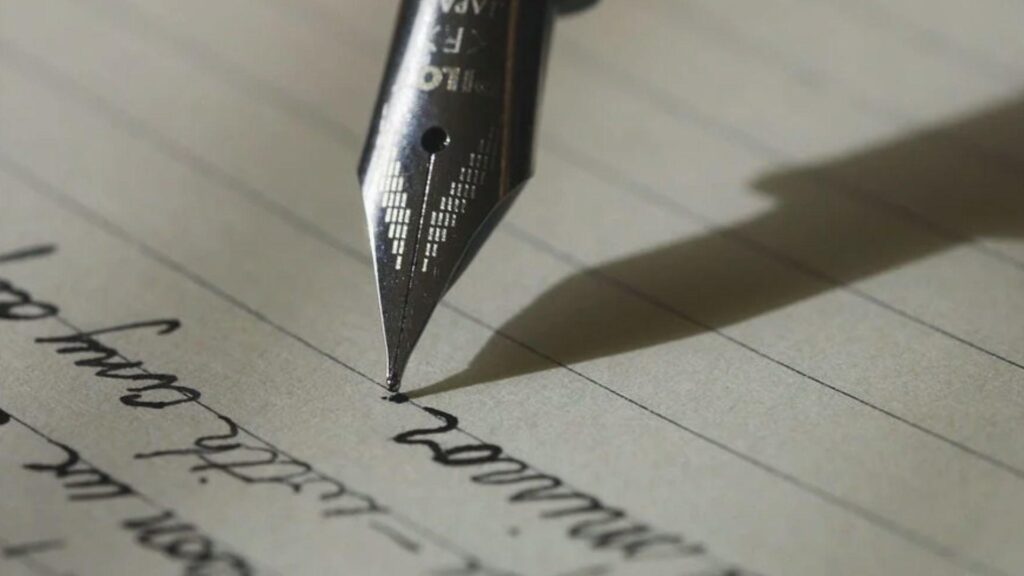 Close-up of a fountain pen nib writing cursive script on lined paper