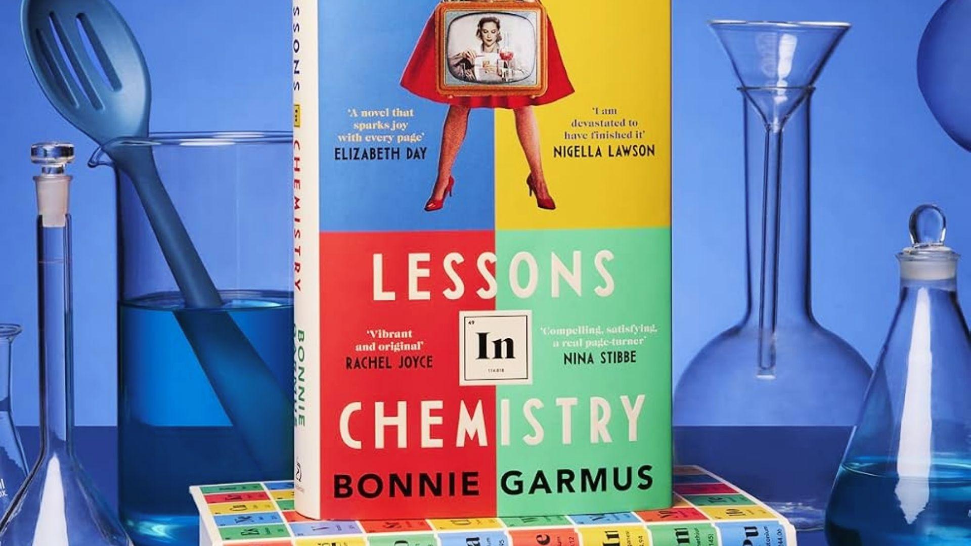 Lessons in Chemistry book displayed among blue laboratory glassware and colorful chemistry-themed blocks
