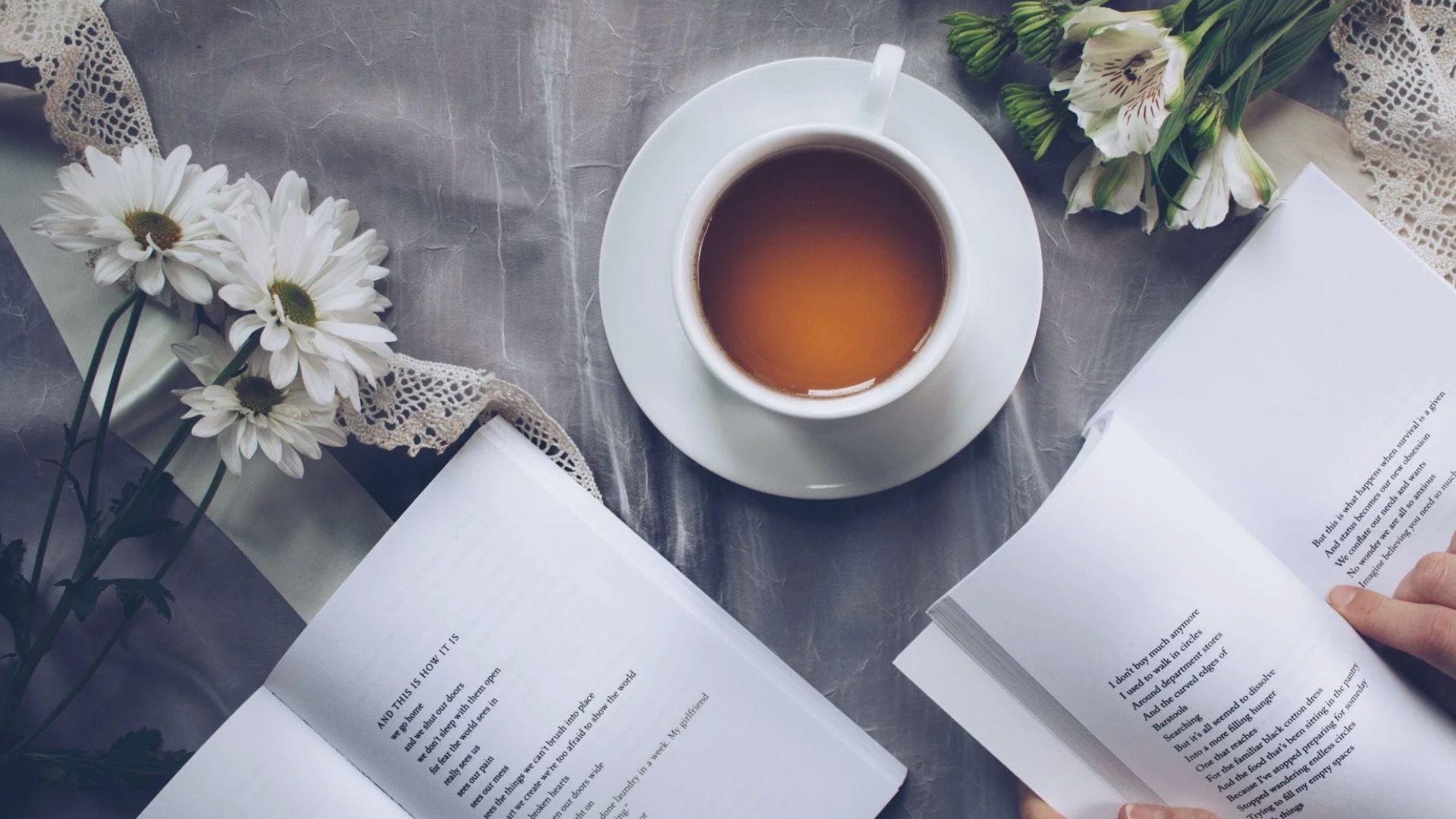 Open poetry books beside a cup of tea and fresh white flowers