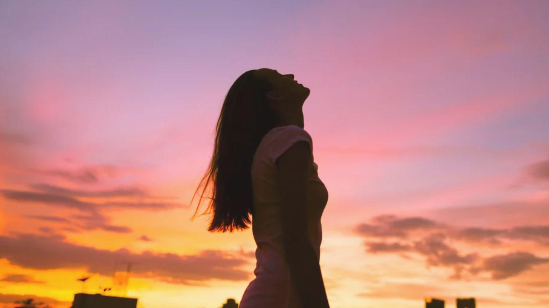 Woman silhouetted against a colorful pink and orange sunset sky
