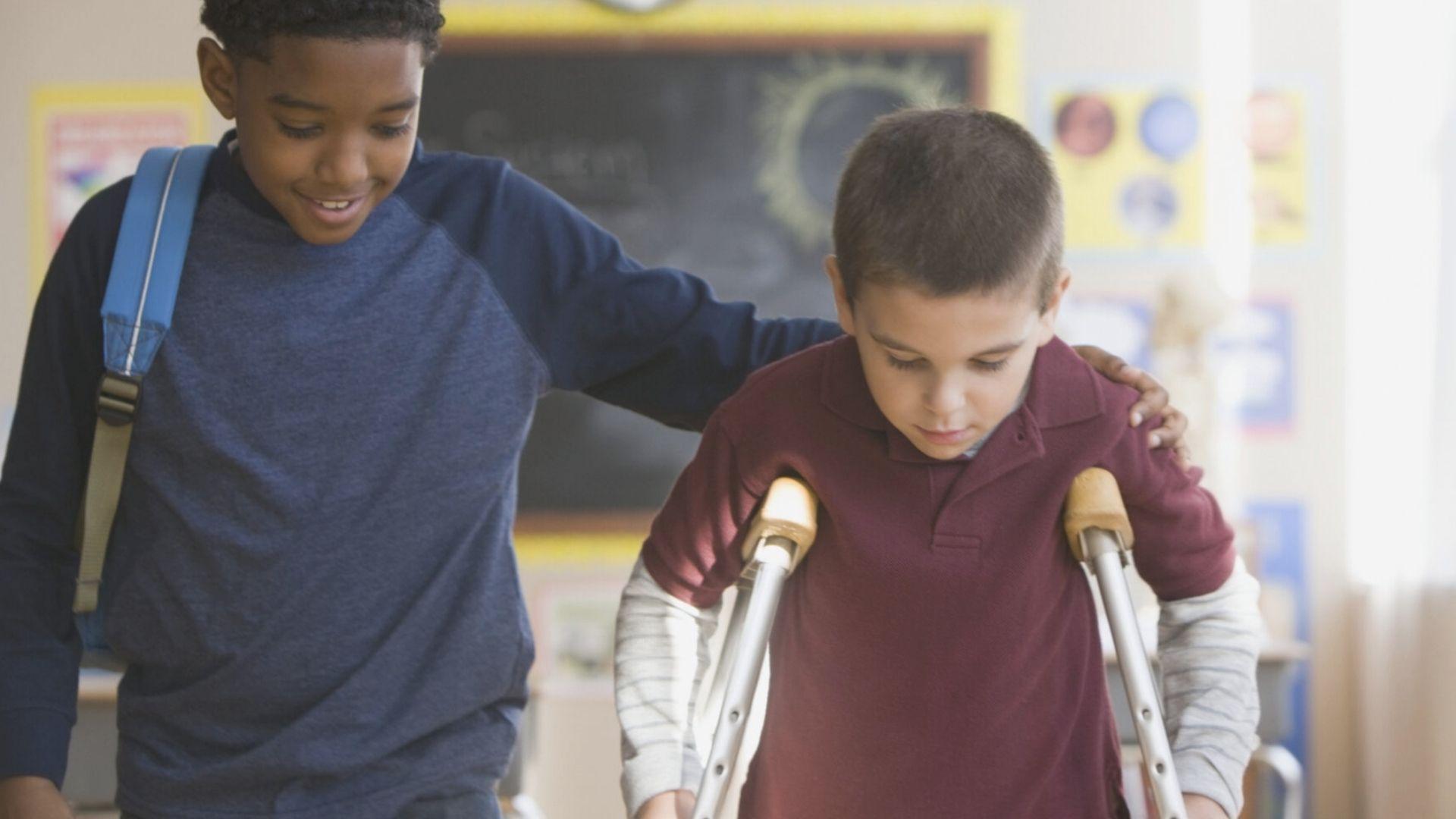 Two schoolboys walking together, one supporting the other with crutches