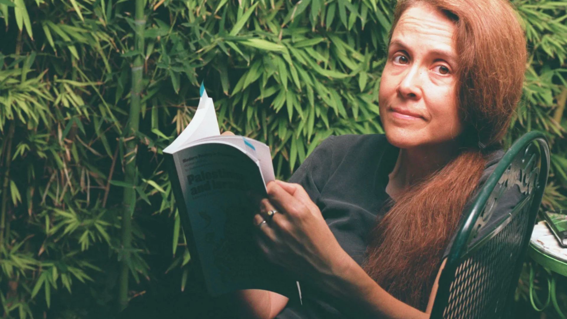 Woman reading a book while sitting outdoors surrounded by bamboo plants