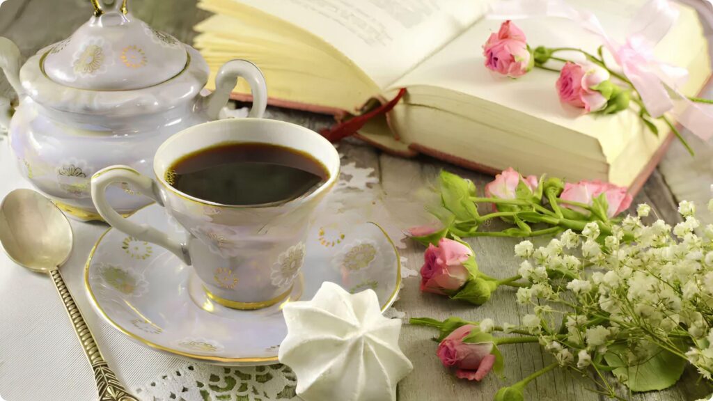 Open book on a table beside a teacup, and flowers on the side. File Name-edward-lear-poems-open-book