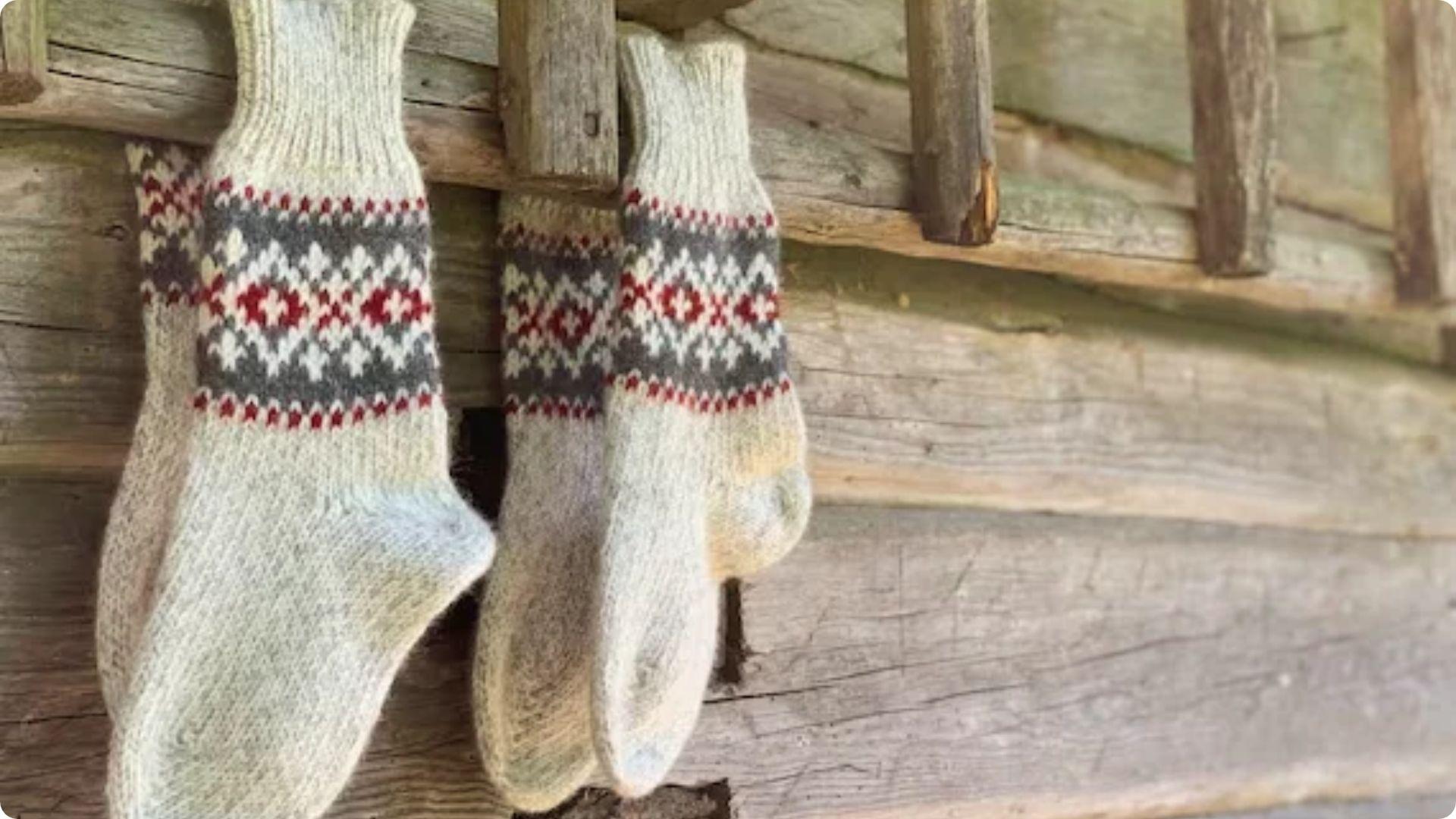 Two pairs of cream woolen socks hanging on a rustic wooden wall outside. File name: ode-to-my-socks-analysis