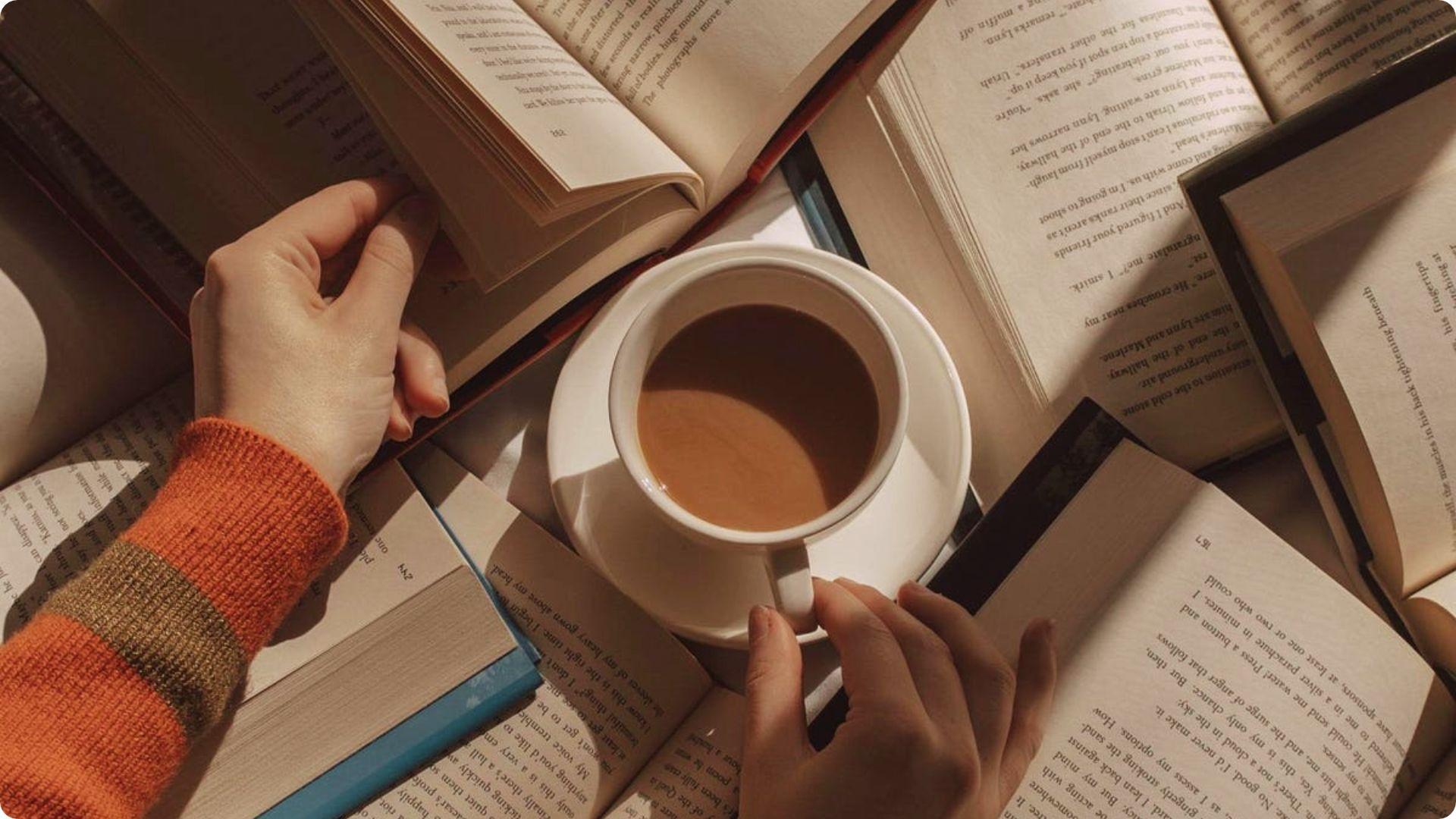 Person's hands holding a book and coffee cup surrounded by open books.File name-best-known-nonsense-songs