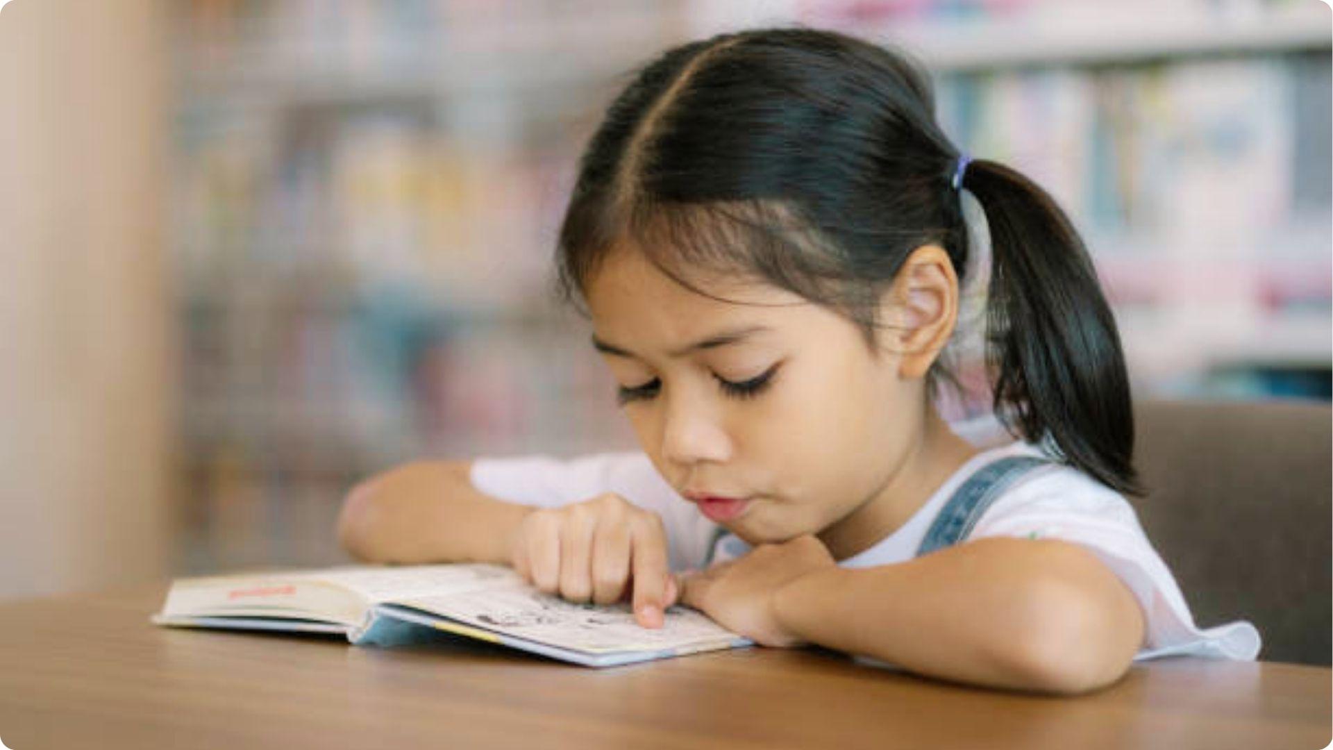 A young girl with a ponytail focused on reading an open book.File name:young-girl-reading