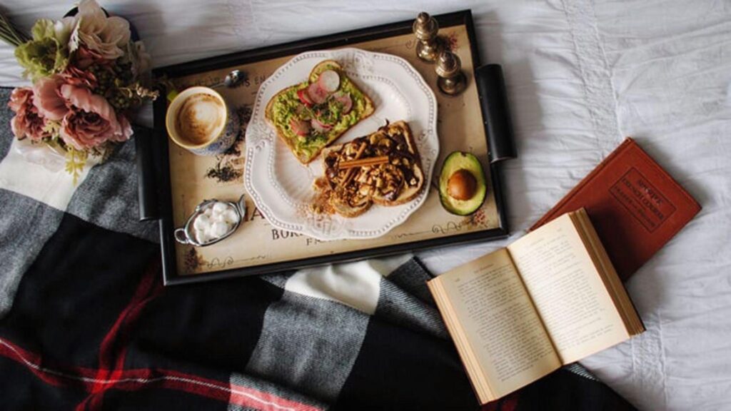 Open book of poems about food beside breakfast on a bed.