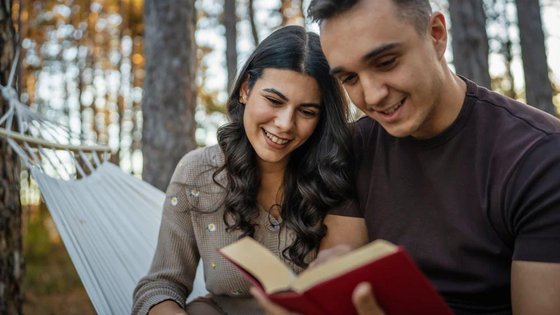 Young couple smiling together reading an open poetry book.